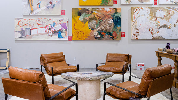 Luxe set of four leather chairs sit around a crystal top coffee table, with fine art hanging on the walls in the background.